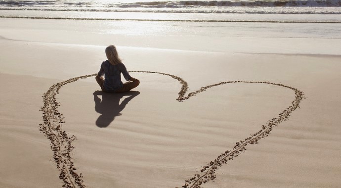 Woman sitting cross-legged in heart on beach